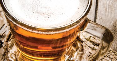 Glass of light beer on a birch stand . On a wooden table.