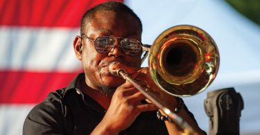 man playing trombone american falg in background